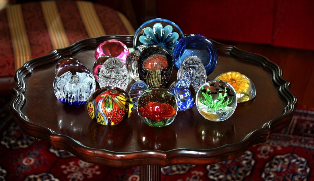 A group of colourful glass paperweights arranged on a scalloped metal tray, their millefiori and floral canes lit from the side.