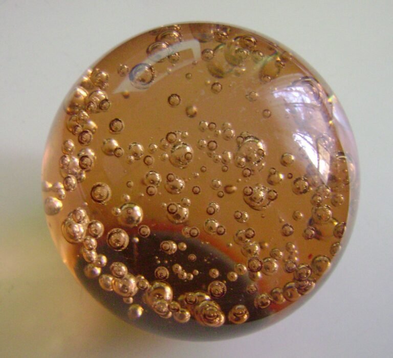 A domed amber glass paperweight seen from above, filled with a rising trail of round air bubbles of varying size.
