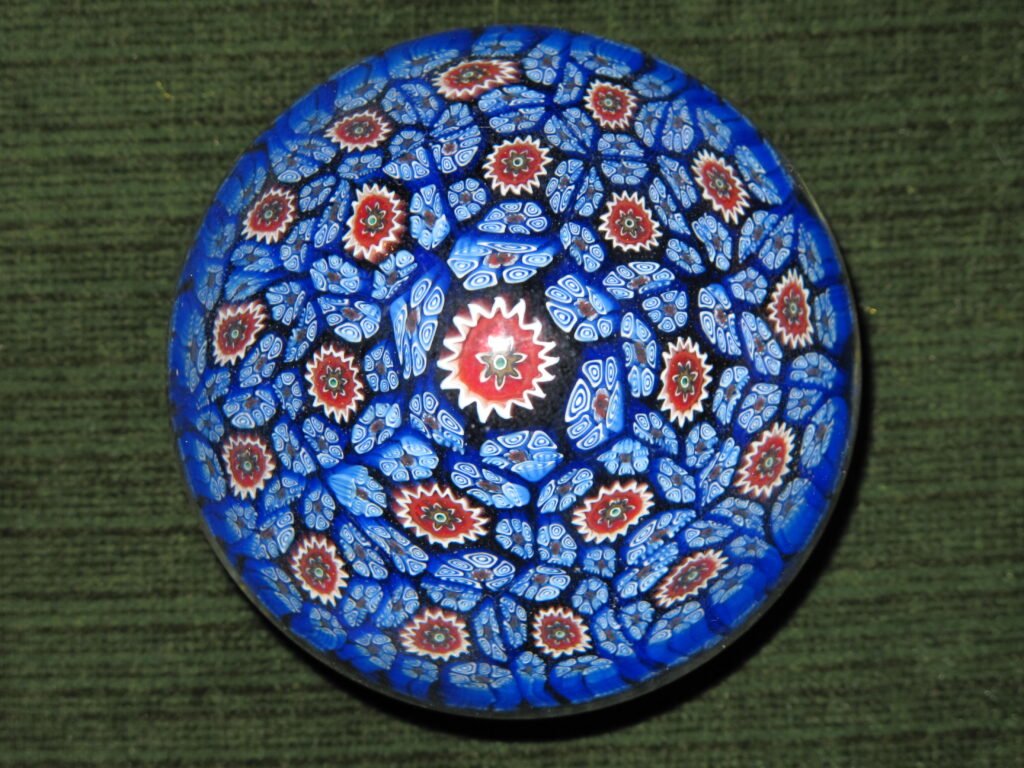A close-packed millefiori paperweight seen from directly above, densely filled with blue and white florets around a single red and white central cane.