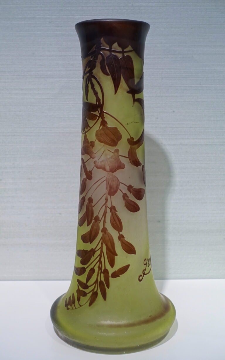 A tall tapering cameo glass vase in pale green, overlaid and carved with brown wisteria blossom and trailing foliage.