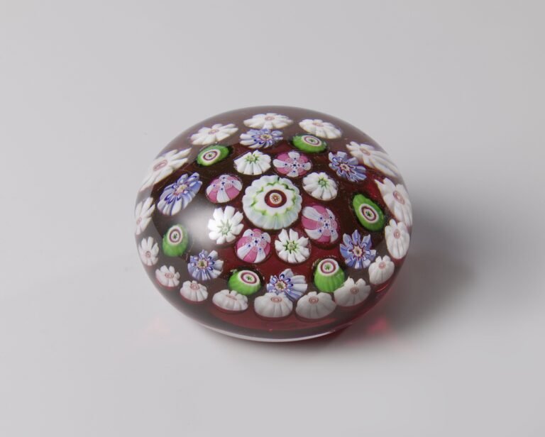 A millefiori paperweight photographed at an angle, showing the clear glass dome curving over an arrangement of pink, green and white canes beneath it.