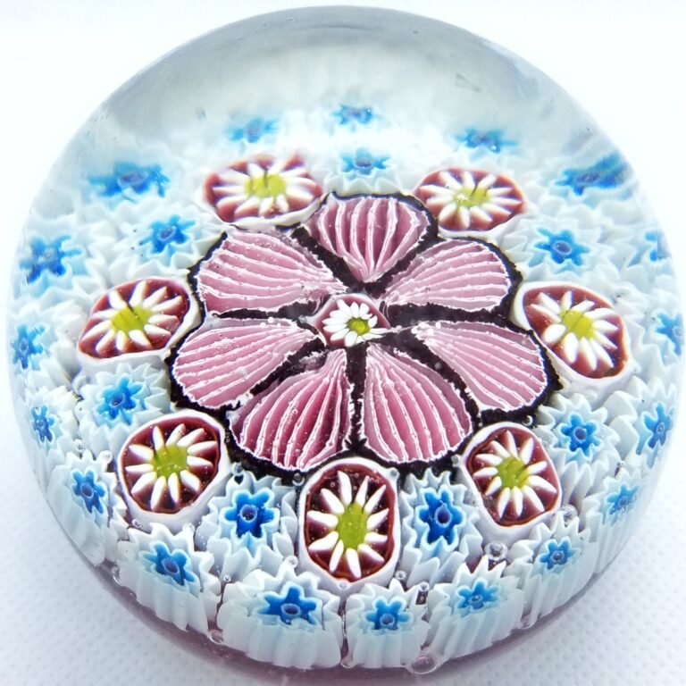 A millefiori paperweight seen from above: a pink and white flower at the centre, ringed by rows of small blue and white canes.