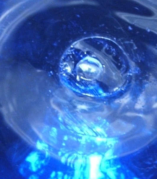 A rough, unpolished pontil scar in the centre of the base of a blue glass bowl, where the working rod was broken away.