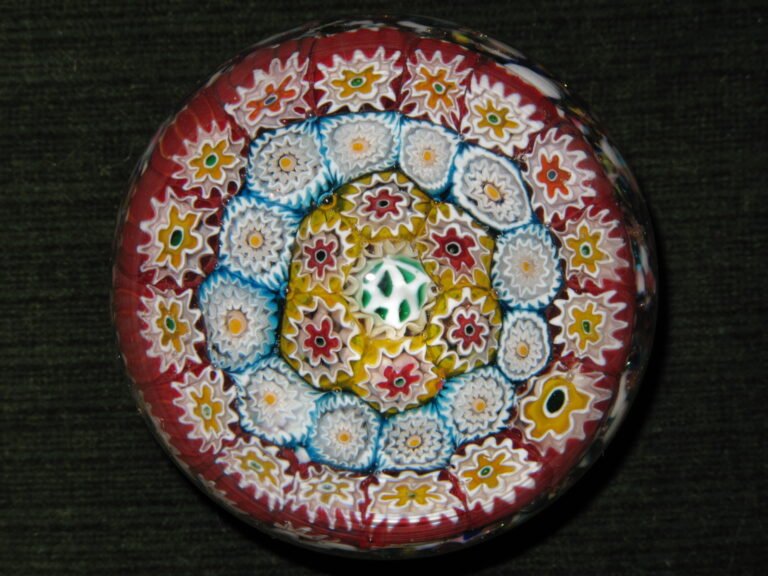 A close-packed millefiori paperweight seen from directly above, with concentric rings of white, yellow and red florets on a deep red ground.