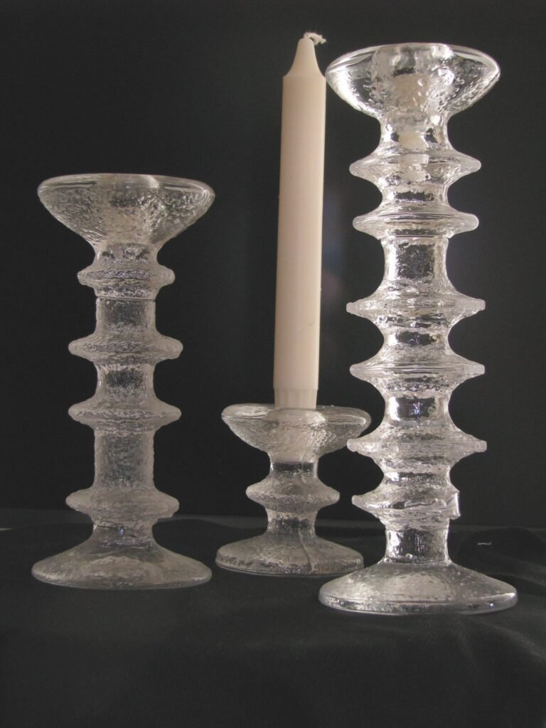 Three clear glass candlesticks of stacked ring form with a rough, icy surface texture, one of them holding a white candle.
